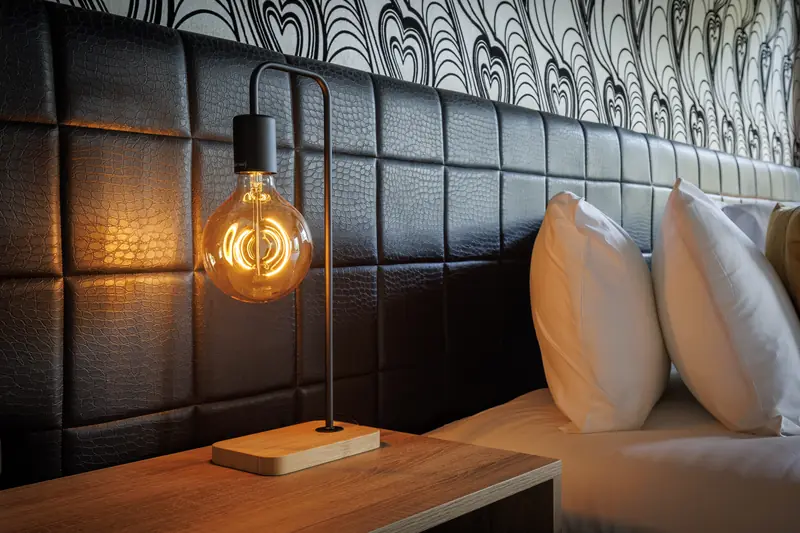 A bedside lamp with a filament bulb against a leather headboard