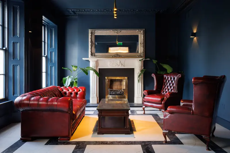 The lounge at The Linn: navy walls, a marble fireplace and red leather Chesterfield sofas