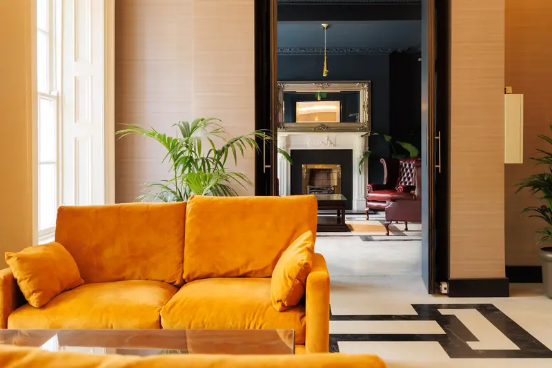 A mustard velvet sofa in the lobby, looking through to the lounge and its fireplace