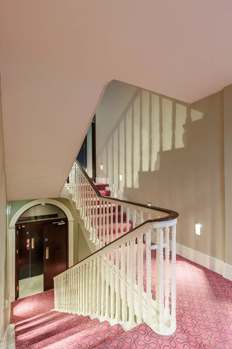 The staircase at The Linn, with white banisters and a red carpet