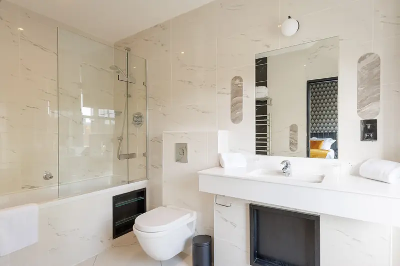 A white marble en-suite bathroom with a bath, shower screen and wide basin