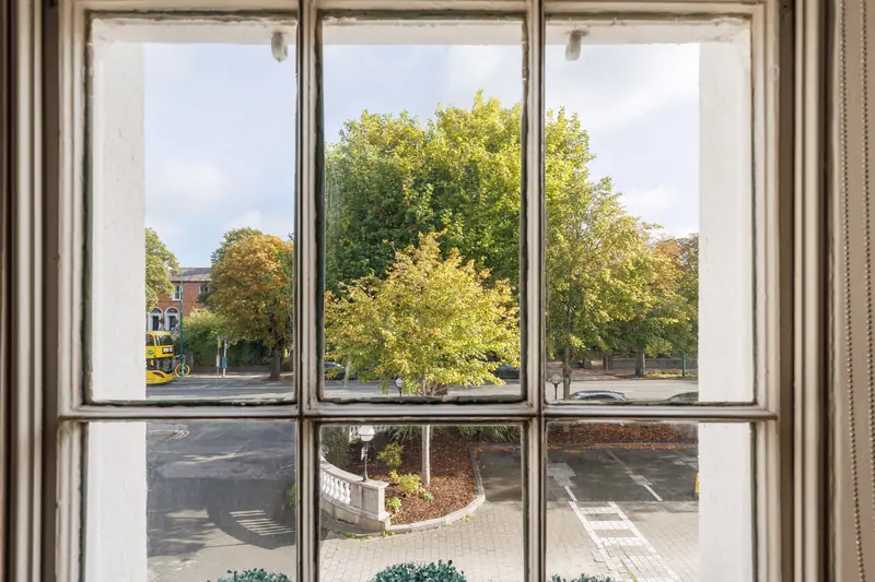 View through a tall sash window at The Linn onto the trees of Morehampton Road